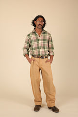A man modeling a green and pink plaid button-down shirt with tan pants, brown shoes, and a brown belt, standing against a solid beige background.