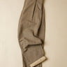A pair of grey pleated trousers with a rolled-up hem showing a lighter beige lining, laid flat against a neutral cream background.