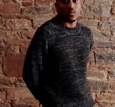 Man wearing a dark sweater standing against a brick wall