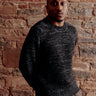 Man wearing a dark sweater standing against a brick wall