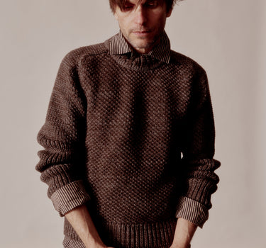 Man wearing a brown knitted sweater against a plain background