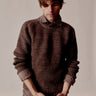 Man wearing a brown knitted sweater against a plain background