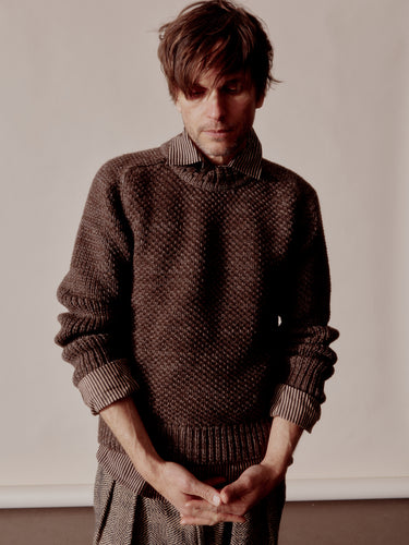 Man wearing a brown knitted sweater against a plain background