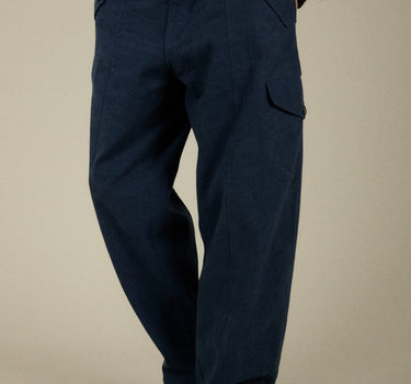 A person wearing dark navy blue cargo-style pants with a matching dark jacket and black shoes, standing against a plain light beige studio background.