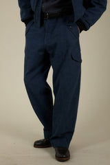 A person wearing dark navy blue cargo-style pants with a matching dark jacket and black shoes, standing against a plain light beige studio background.