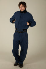 A man modeling a dark navy blue heavy-duty workwear set consisting of a cropped jacket with black ribbed collar and cuffs, and matching dark blue trousers, against a plain beige studio background.