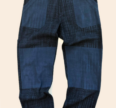 A pair of handwoven cotton pants featuring a hand embroidered running stitch pattern with indigo and iron space dyes, and contrasting fabric double knee and patch pockets.
