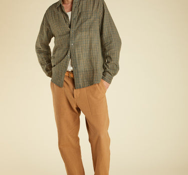 Man wearing a green checkered shirt, brown pants, and brown shoes on a beige background