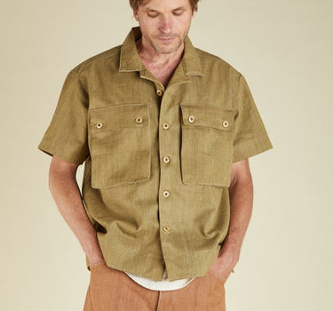 Man wearing a green short-sleeve shirt with button details on a beige background