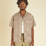 Man wearing a striped shirt and beige pants against a beige background