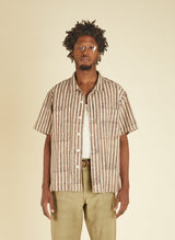 Man wearing a striped shirt and beige pants against a beige background