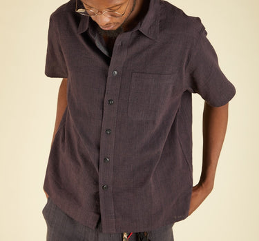 Person wearing a dark plum button-up shirt and pants on a beige background