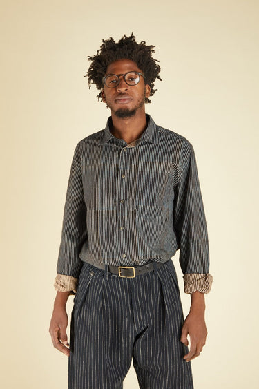 Man wearing a striped shirt and pants with a belt on a beige background