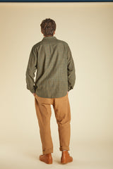 Person wearing a green checkered shirt and brown pants on a beige background