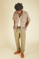 Person wearing a striped shirt, beige pants, and brown shoes on a beige background