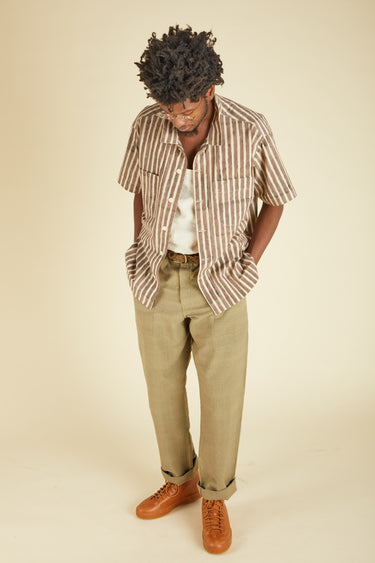 Person wearing a striped shirt, beige pants, and brown shoes on a beige background