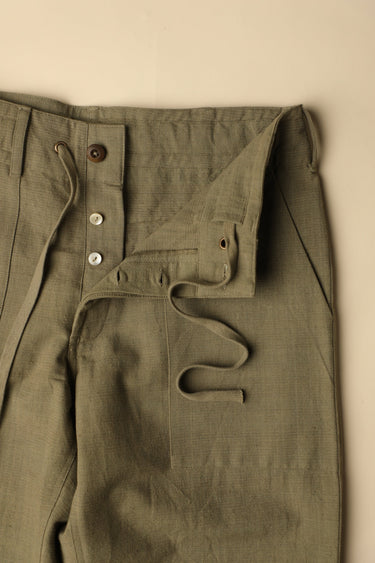 Close-up of olive green pants with buttons on a beige background