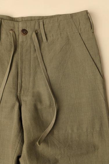 Close-up of olive green pants with a beige background