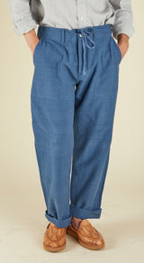 Person wearing blue pants with a drawstring and a light gray shirt on a beige background