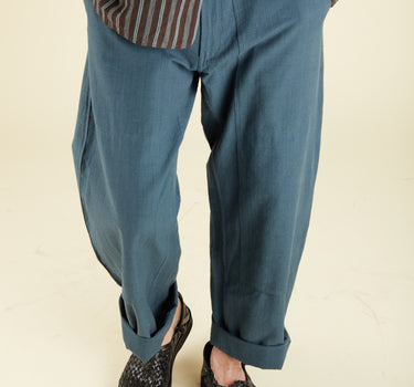 Person wearing teal blue pants and a striped shirt on a plain background