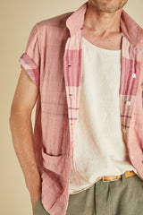 Man wearing a pink plaid shirt over a white tank top with a beige background