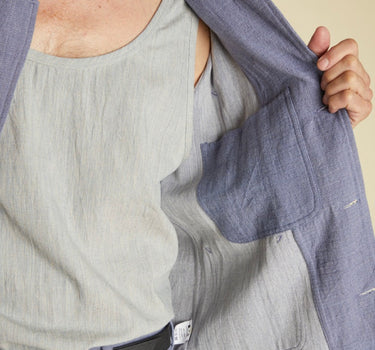 Person wearing a light gray tank top and blue jacket on a beige background