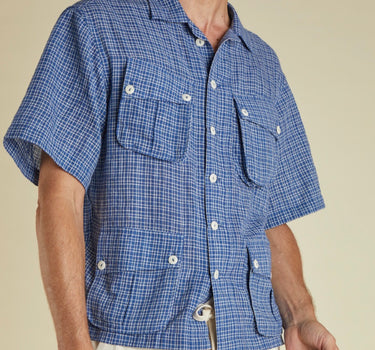 Man wearing a blue checkered shirt with short sleeves against a beige background