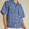 Man wearing a blue checkered shirt with short sleeves against a beige background