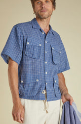 Man wearing a blue checkered shirt with short sleeves against a beige background