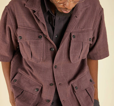 Person wearing a brown short-sleeve jacket with multiple pockets on a beige background