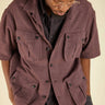 Person wearing a brown short-sleeve jacket with multiple pockets on a beige background