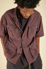 Person wearing a brown short-sleeve jacket with multiple pockets on a beige background